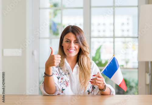 Young woman at home holding flag of France happy with big smile doing ok sign, thumb up with fingers, excellent sign