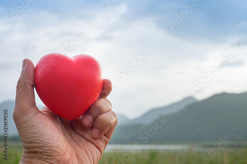 Man Hand holding Red Heart shape rubber model with outdoor mountain background.Image Concept good health.