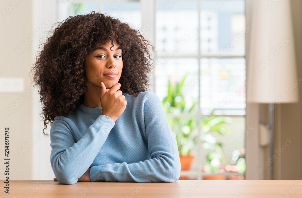 African american woman at home looking confident at the camera with smile with crossed arms and hand raised on chin. Thinking positive. African american woman at home looking confident at the camera with smile with crossed arms and hand raised on chin. Thinking positive.