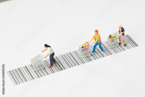 Miniature people figurine with grocery in the shopping cart rally on the bar code using as ecommerce, consumer or buy and sale in new technology channel concept