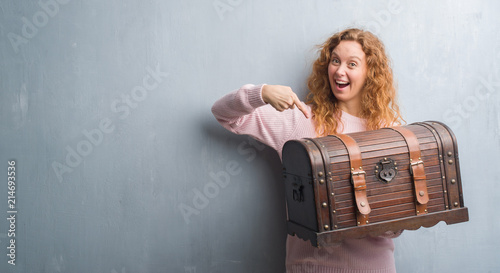 Fotografía Young redhead woman holding vintage chest very happy pointing with hand and fing
