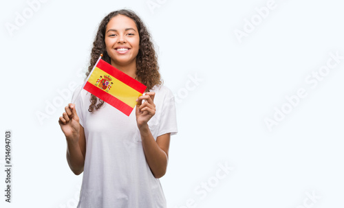 Young hispanic woman holding flag of Spain with a happy face standing and smiling with a confident smile showing teeth