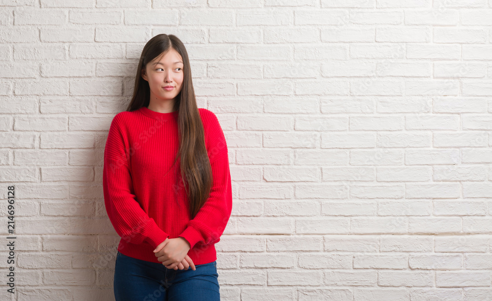 Young Chinese woman over brick wall smiling looking side and staring away thinking. Young Chinese woman over brick wall smiling looking side and staring away thinking.