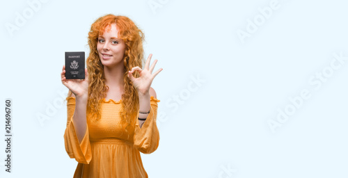 Young redhead woman holding passport of United States of America doing ok sign with fingers, excellent symbol