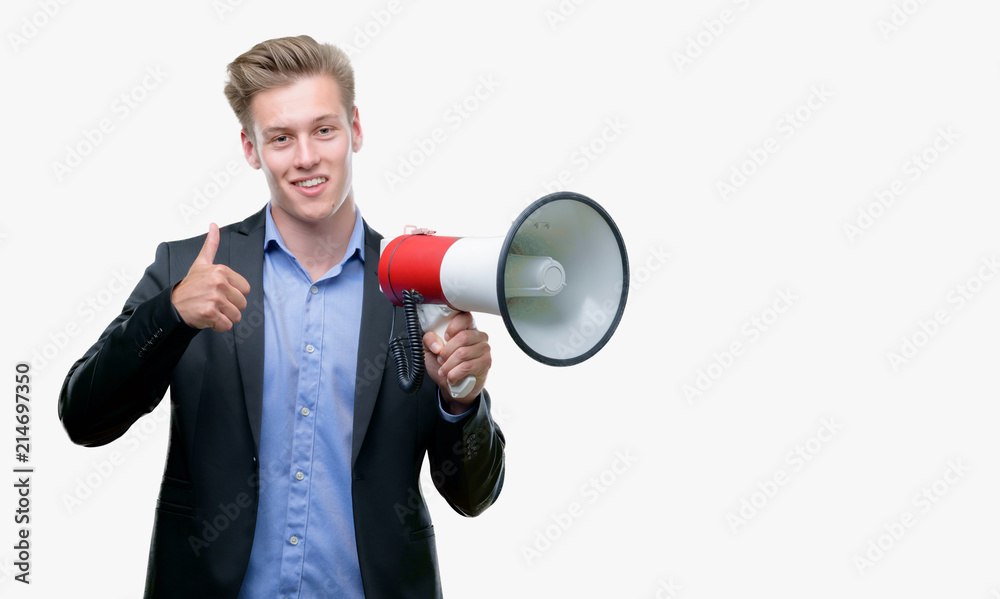 Young handsome blond man holding a megaphone happy with big smile doing ok sign, thumb up with fingers, excellent sign