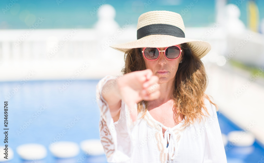 Middle age brunette woman by the swiming pool with angry face, negative sign showing dislike with thumbs down, rejection concept