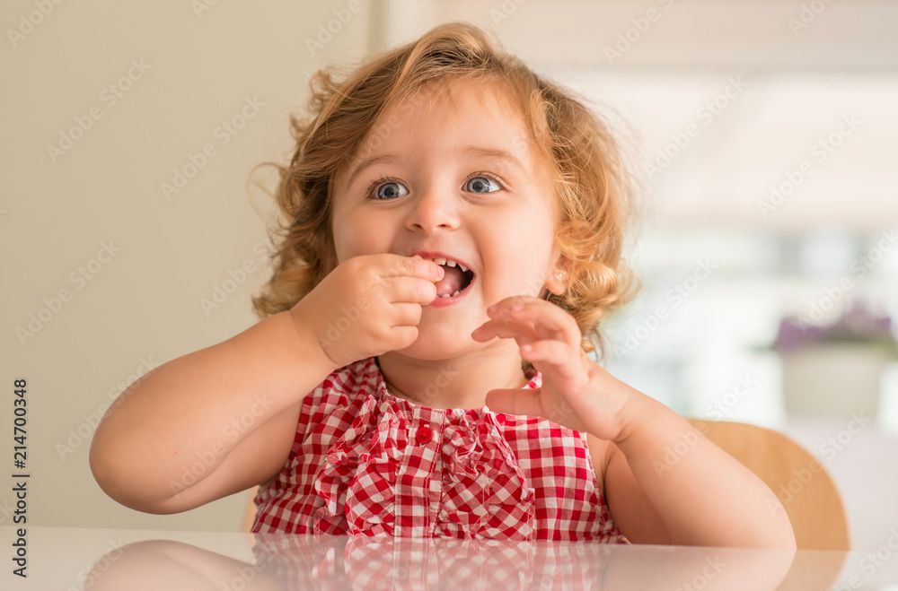 Beautiful blonde child with blue eyes smiling and eating candy at home. Beautiful blonde child with blue eyes smiling and eating candy at home.
