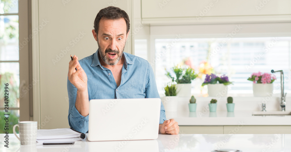 Middle age man using laptop at home scared in shock with a surprise face, afraid and excited with fear expression