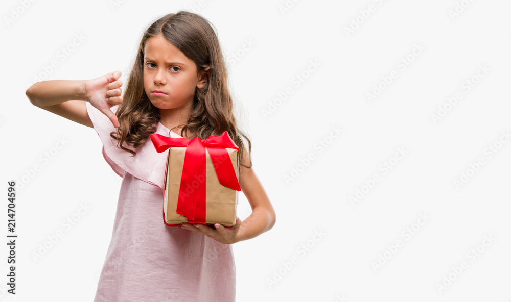 Brunette hispanic girl holding a gift with angry face, negative sign showing dislike with thumbs down, rejection concept Brunette hispanic girl holding a gift with angry face, negative sign showing dislike with thumbs down, rejection concept