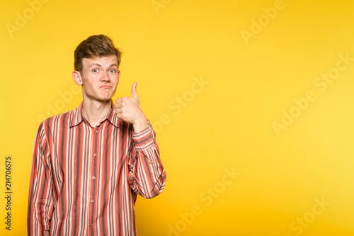 approving smiling man showing a thumb up gesture. portrait of a young guy on yellow background. copyspace for advertisement.