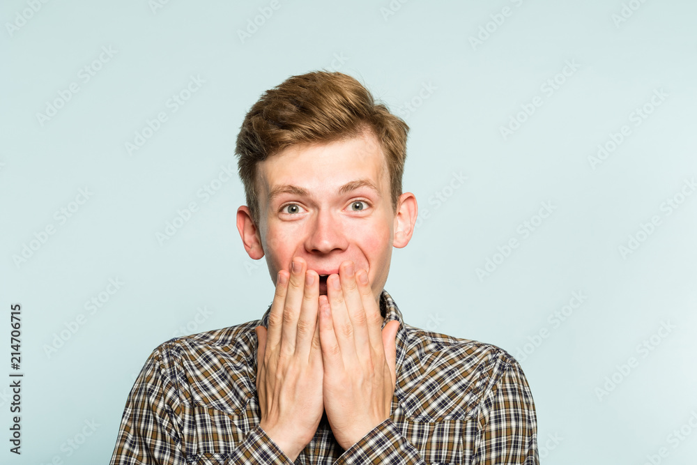 joyful excited happy smiling man covering mouth with hands. portrait of a young guy on light background. emotion facial expression. feelings and people reaction. joyful excited happy smiling man covering mouth with hands. portrait of a young guy on light background. emotion facial expression. feelings and people reaction.