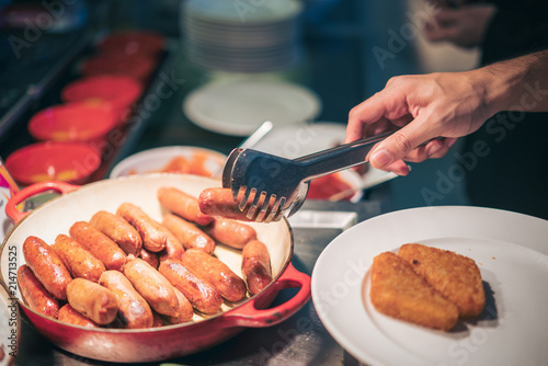 Man hand pick sausage into plate in breakfast at hotel