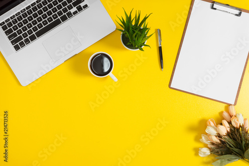 Laptop and clipboard on yellow background. Elegant work space flat lay.