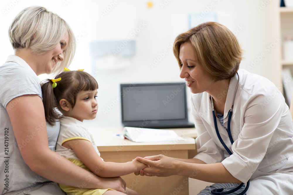 Pediatrician female doctor holding child's hand in her hands. Little girl sitting at mother's knees Pediatrician female doctor holding child's hand in her hands. Little girl sitting at mother's knees