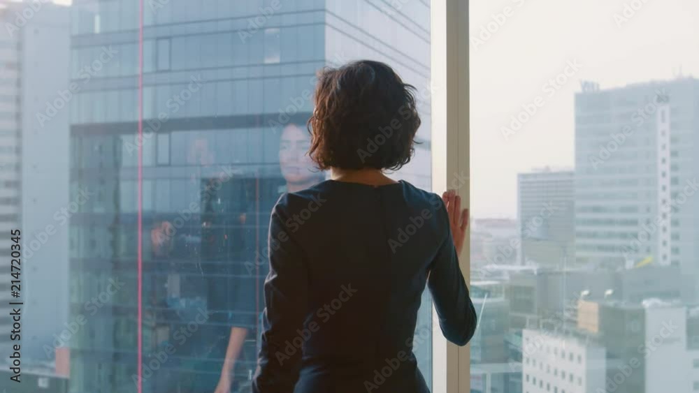 Following Shot of the Successful Businesswoman in a Stylish Dress Walking Through Her Office and Looking out of the Window Thoughtfully. 