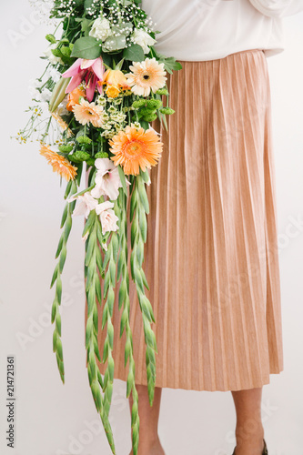 Woman in pinkish beige pleated skirt holds a muted orange themed summer bouquet. photo
