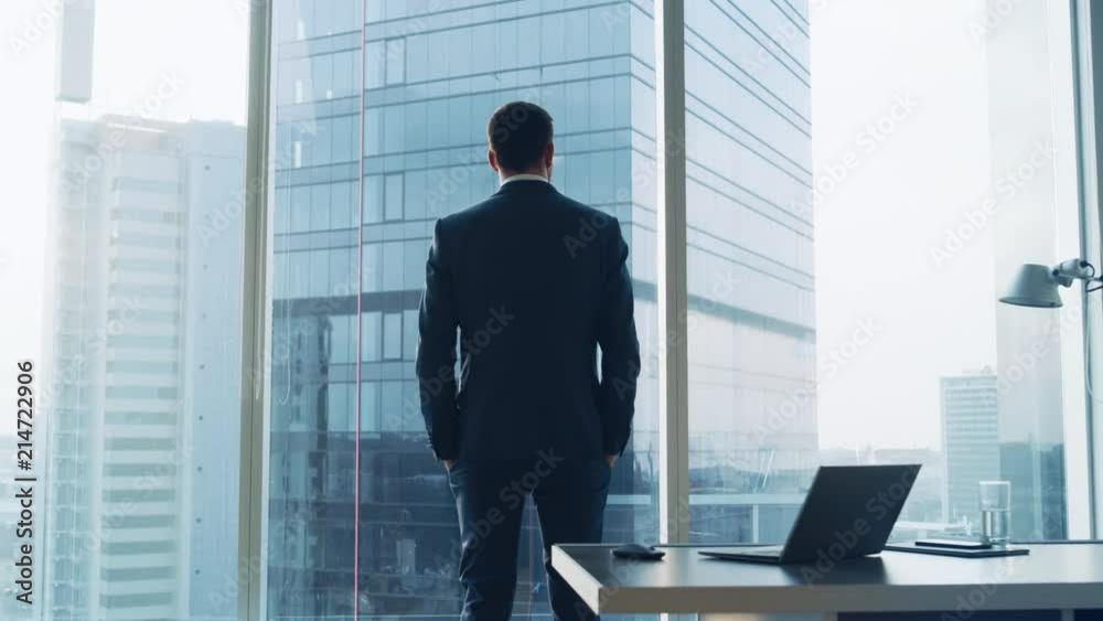 Back View of the Thoughtful Businessman wearing a Suit Standing in His Office, Hands in Pockets and Contemplating. Shot on RED EPIC-W 8K Helium Cinema Camera.