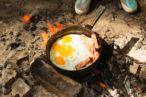 Scrambled eggs with bacon on the cast-iron pan on a bonfire, top view.