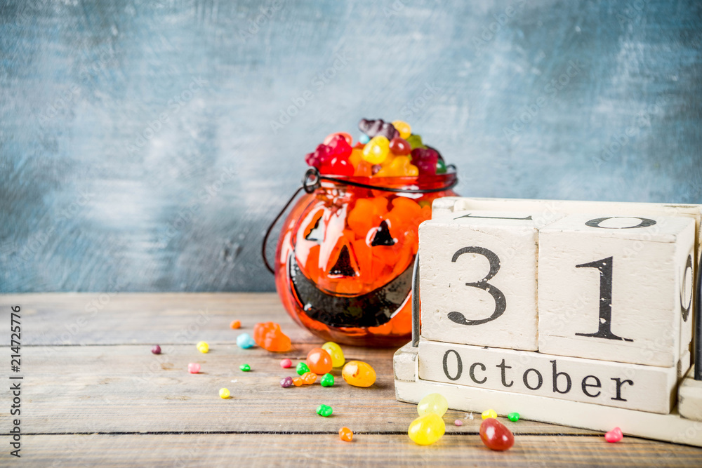 Halloween celebration concept with pumpkin decoration, candy, jack o lantern cup and old retro styled wooden calendar, blue and wooden background, copy space