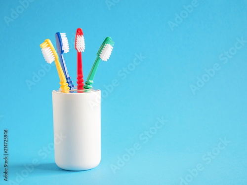 four colored toothbrushes in a glass on a light blue background 