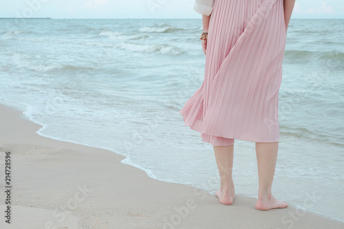 Legs of woman relax in pink dress on a beach sea sand and wave in summer.