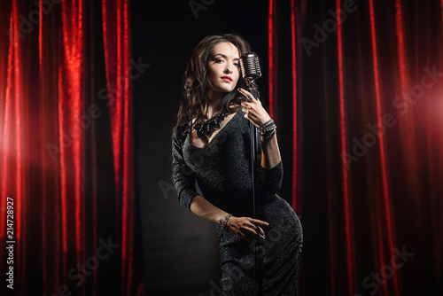 Young beautiful singer in black dress posing with microphone