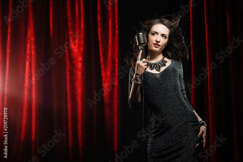 Beautiful girl in black dress singing in the microphone in the concert hall