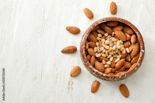 Bowl with different nuts on white wooden background