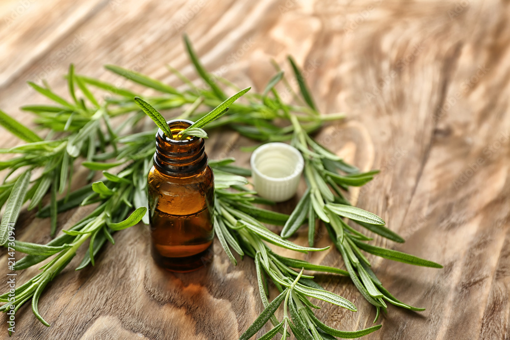 Fresh rosemary and bottle of essential oil on wooden background Fresh rosemary and bottle of essential oil on wooden background
