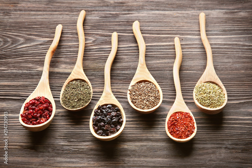 Spoons with different dry spices on wooden background