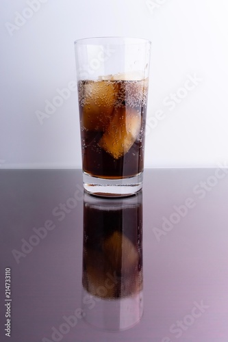 Cola and ice cubes in glass on white background with selective focus and crop fragment