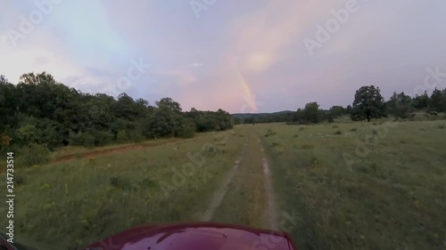 Off road car follow a dirt road towards to rainbow