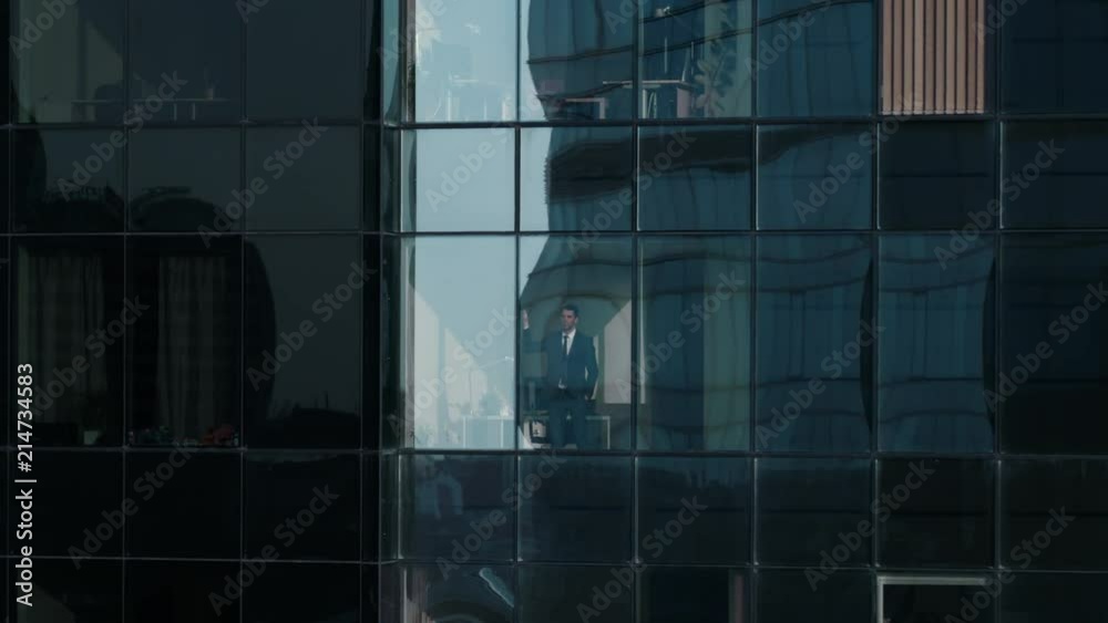 Aerial View Footage: From Outside into Office Building with Businessman Working and Looking out of the Window. Beautiful Flying Zoom Out Shot of The Financial Business District Skyscrapers. 