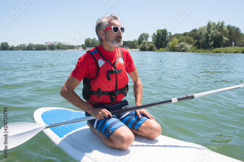 mature attractive rider contemplating nature sitting on paddle board