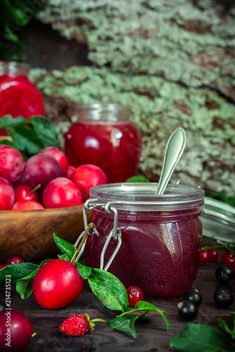 assortment of jam in glass jars, seasonal fresh berries and fruit plum, strawberry, currant, raspberries on a dark background selective focus with copy space, crop concept