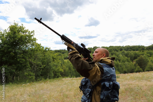 Hunting season. Male 35-40 years old, a hunter is aiming at the sky from a firearm in a clearing in the forest.