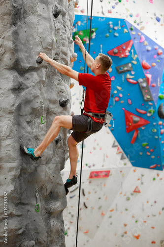 Photo from back of sports guy in red T-shirt training on climbing wall