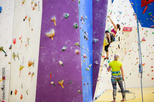 Photo of young sports girl exercising on climbing wall with trainer © Sergey