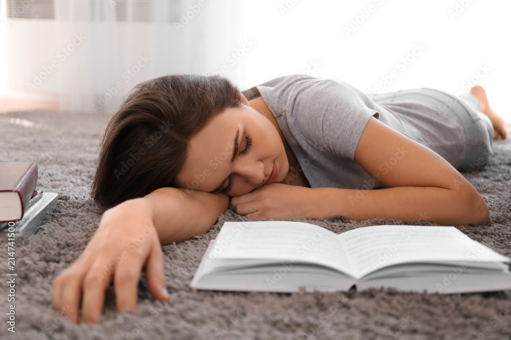 Tired young woman with book sleeping on carpet at home Tired young woman with book sleeping on carpet at home