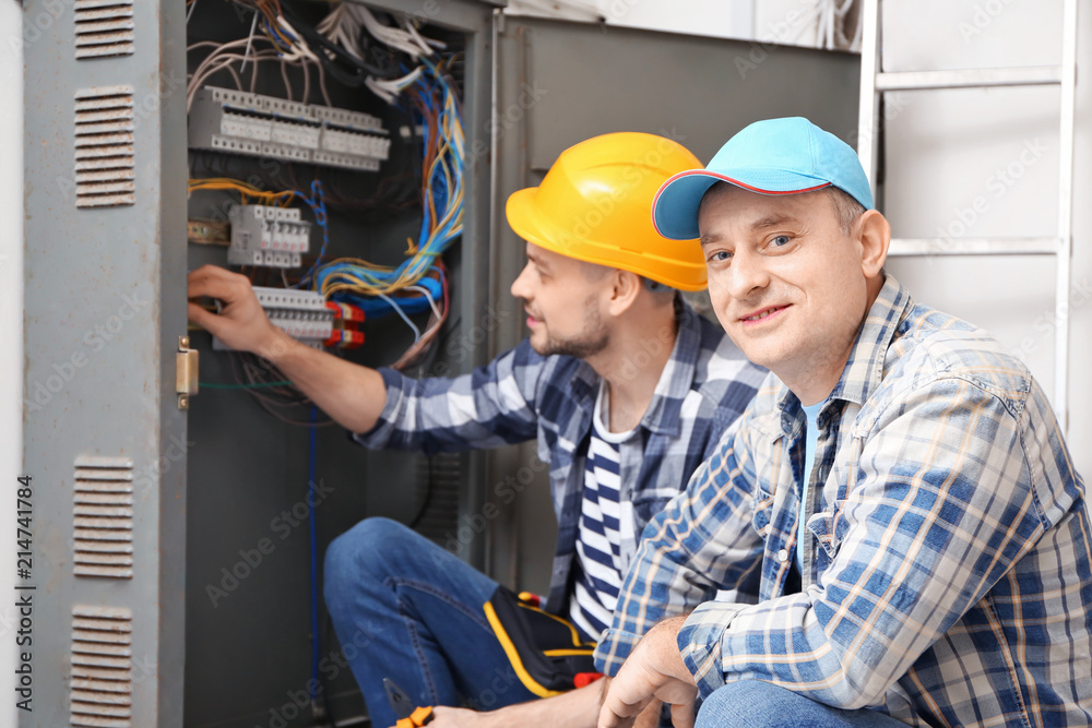 Two electricians near distribution board indoors Two electricians near distribution board indoors