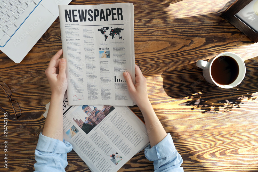 Naklejka premium Young woman reading newspaper at table