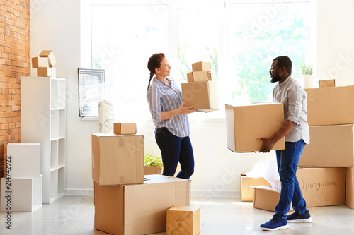 Interracial couple carrying boxes indoors. Moving into new house
