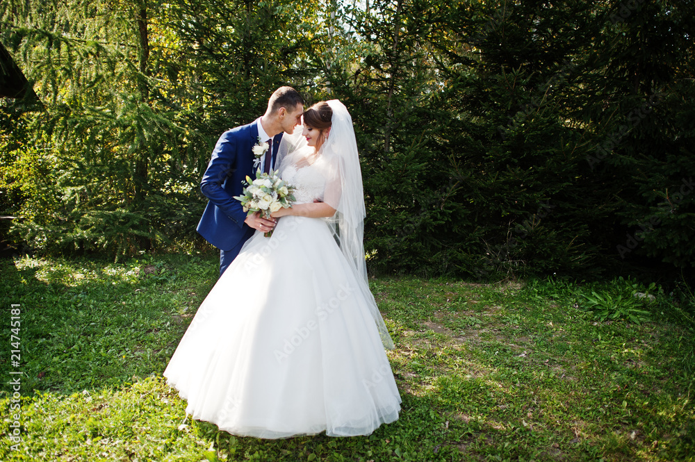 Happy newly married couple posing outdoors in the garden or park next to the wooden gazebo on their wedding day.