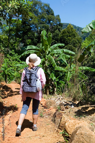 A girl with a backpack walks through the jungle.