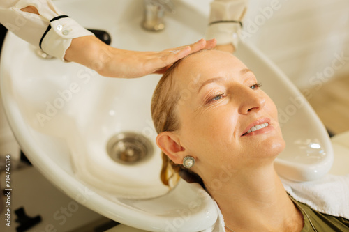 Hair washing. Delighted nice woman smiling while enjoying the procedure of hair washing