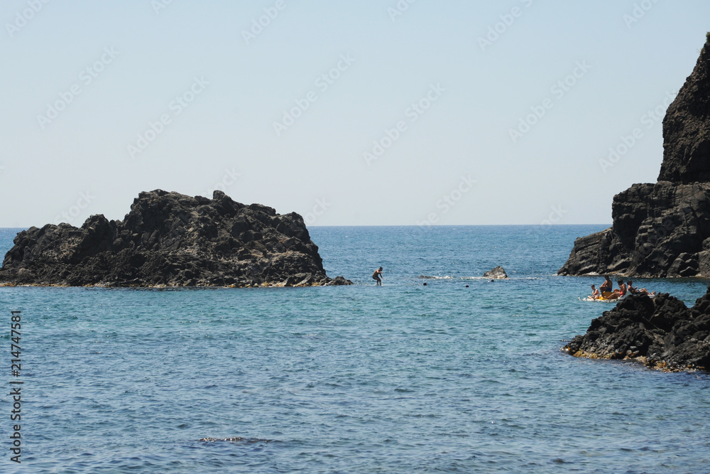 View on the rocky islands in Aci Trezza, Sicily, Italy, with the Islands of the Cyclops in the background.
