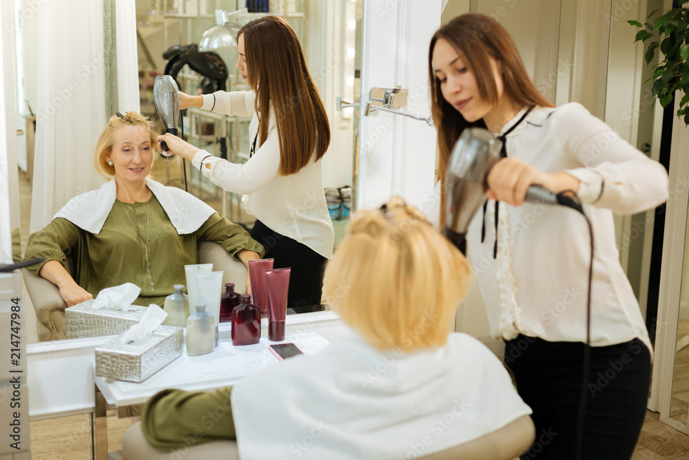 New hairstyle. Nice positive woman looking into the mirror while observing the process of making a new hairstyle New hairstyle. Nice positive woman looking into the mirror while observing the process of making a new hairstyle