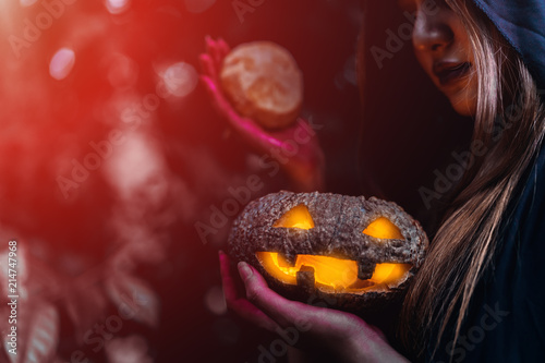 Witch holding pumpkin carved halloween horror concept, psychopomp evil wicked costume at dark forest with copy space the left. photo