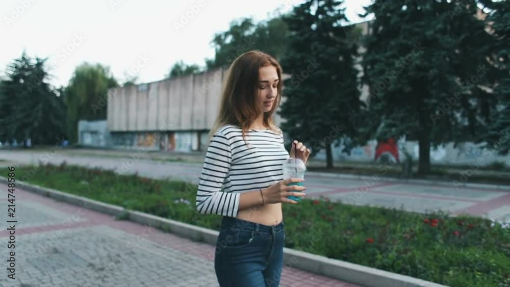 stylish beautiful girl in tops and jeans drinks a summer drink walking through the city park stylish beautiful girl in tops and jeans drinks a summer drink walking through the city park