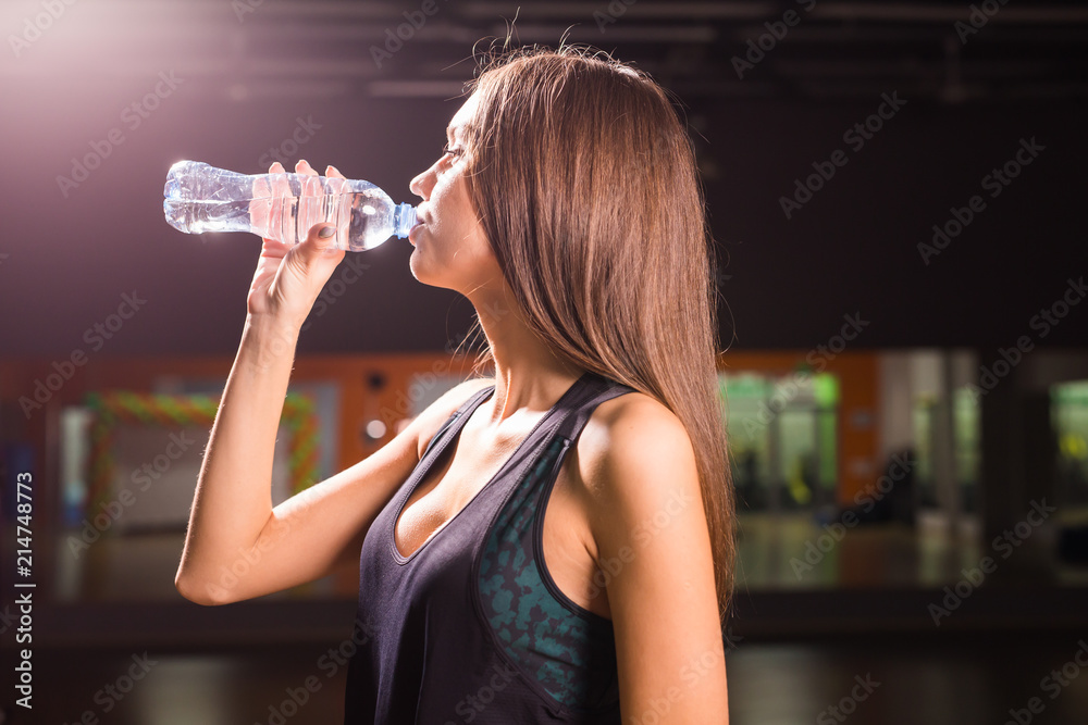 Fitness woman drinking water from bottle. Muscular young female at gym taking a break from workout. Fitness woman drinking water from bottle. Muscular young female at gym taking a break from workout.